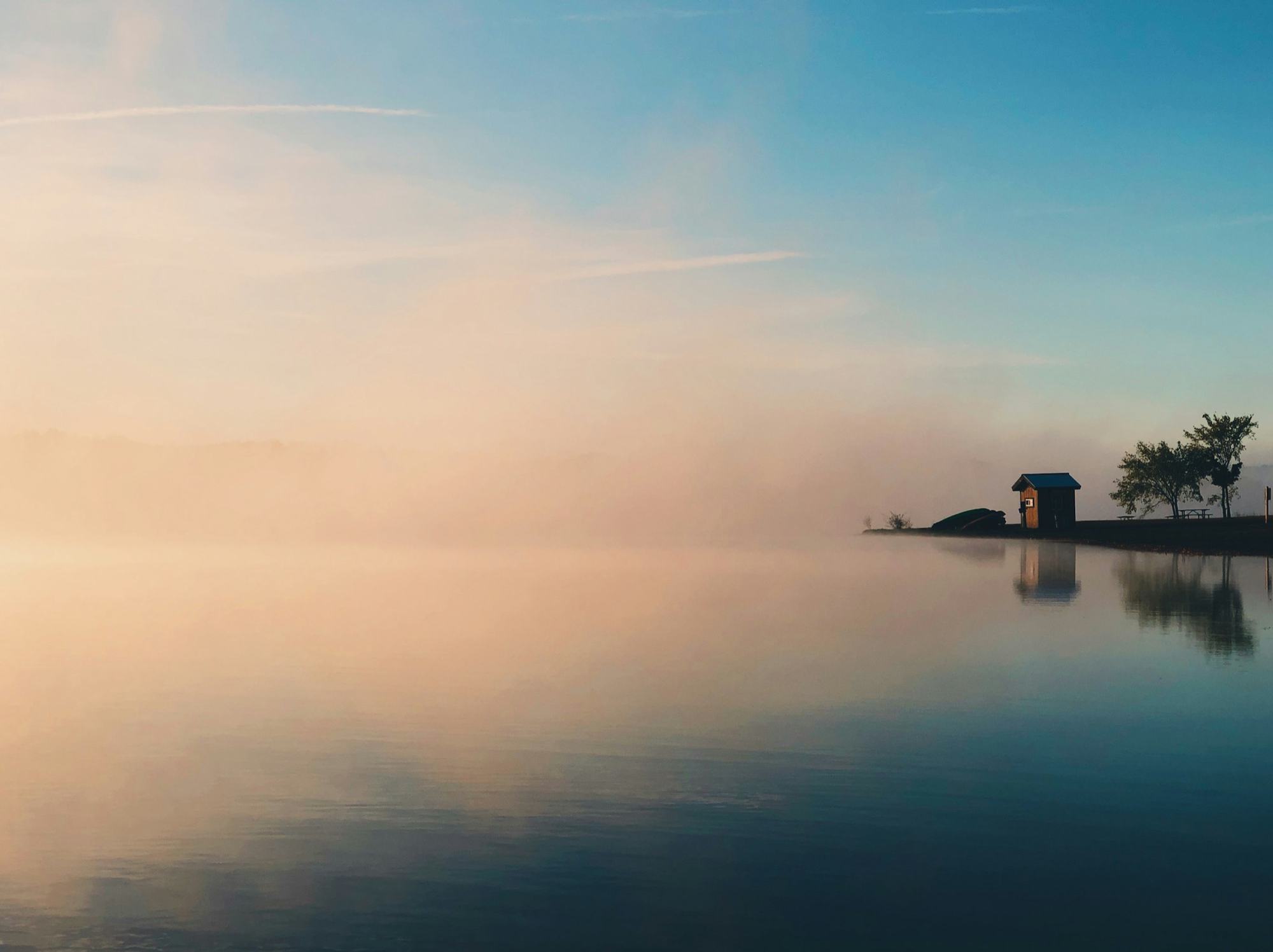 Morning mist over still water with a small cottage on a point