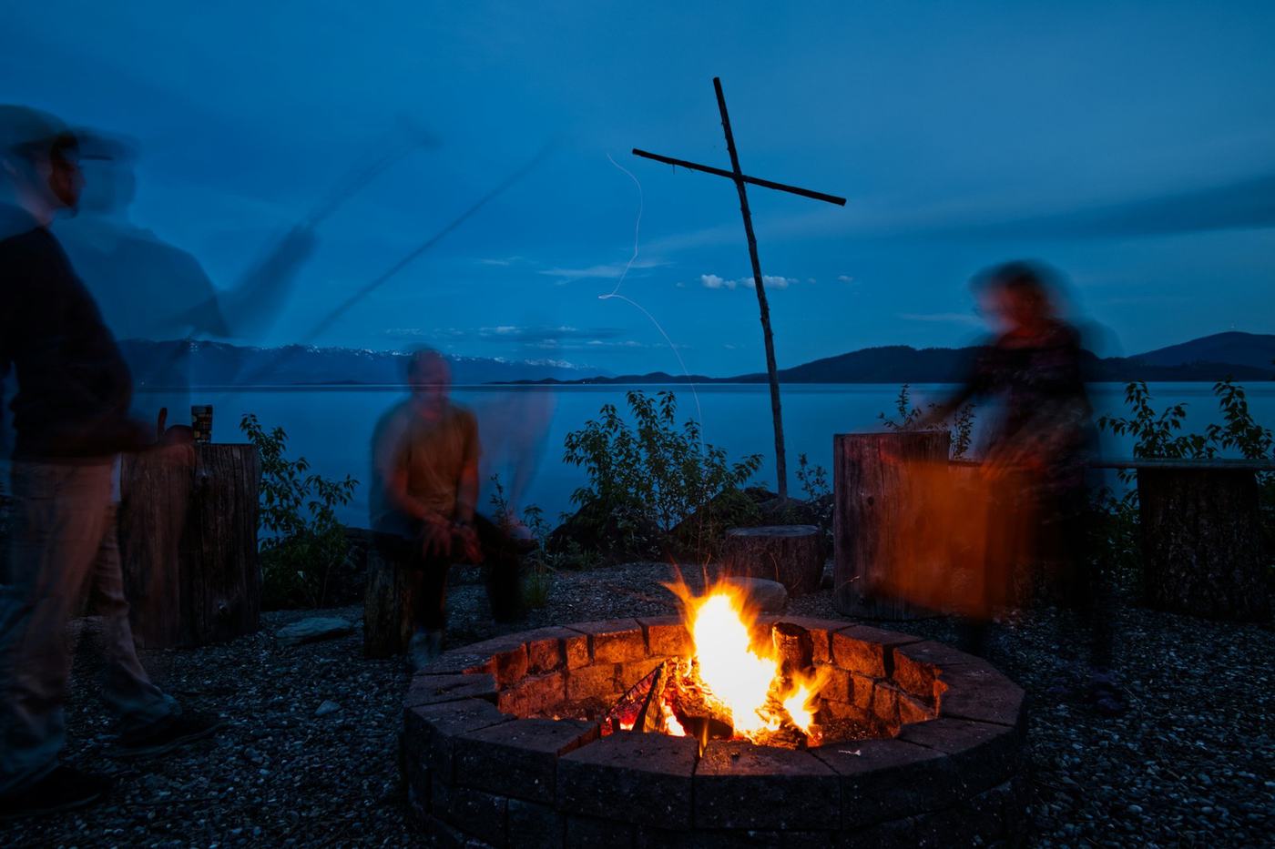 Guests gathered around a stone fire pit on the shore at dusk