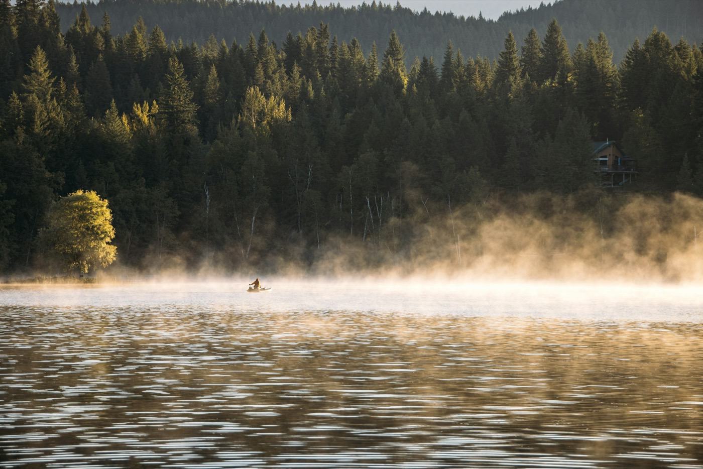 Kayaker on a misty lake at sunrise